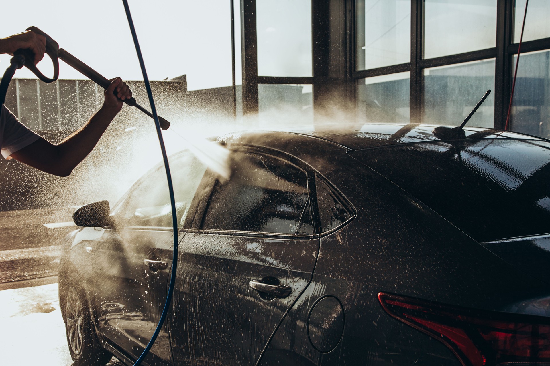 A man washes his car at a self-service car wash using a hose with pressurized water